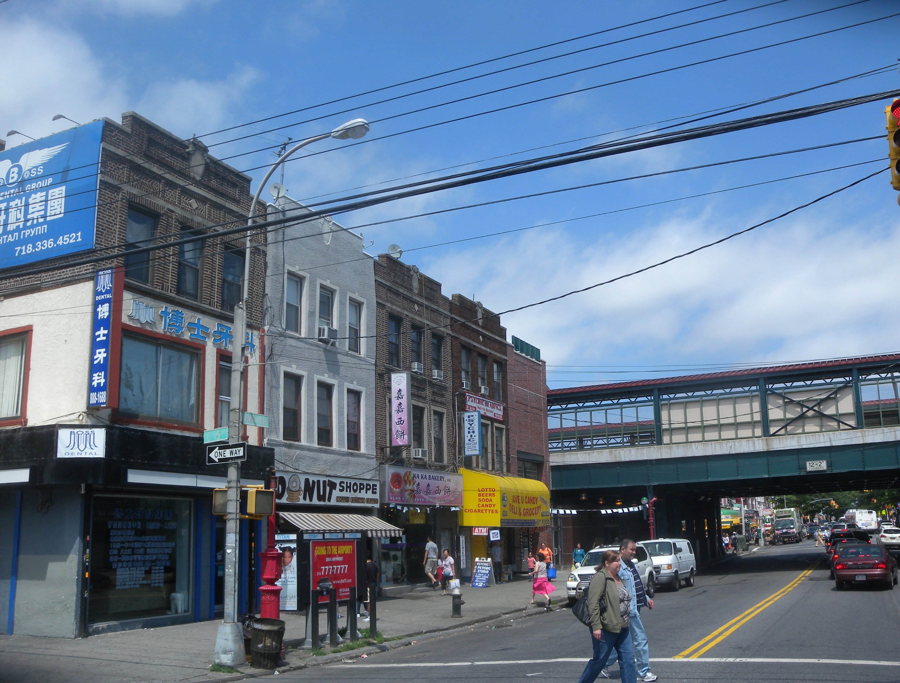 Avenue U commercial corridor beneath the elevated tracks — donut shop, Chinese bakery, Ave U Candy Deli & Grocery